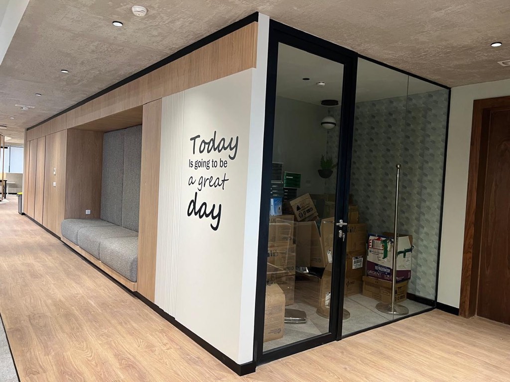 Box acoustique fermé par une menuiserie vitrée, bardage mural en bois et assise intégrée dans un plateau de bureaux, réalisation TG2A 23
