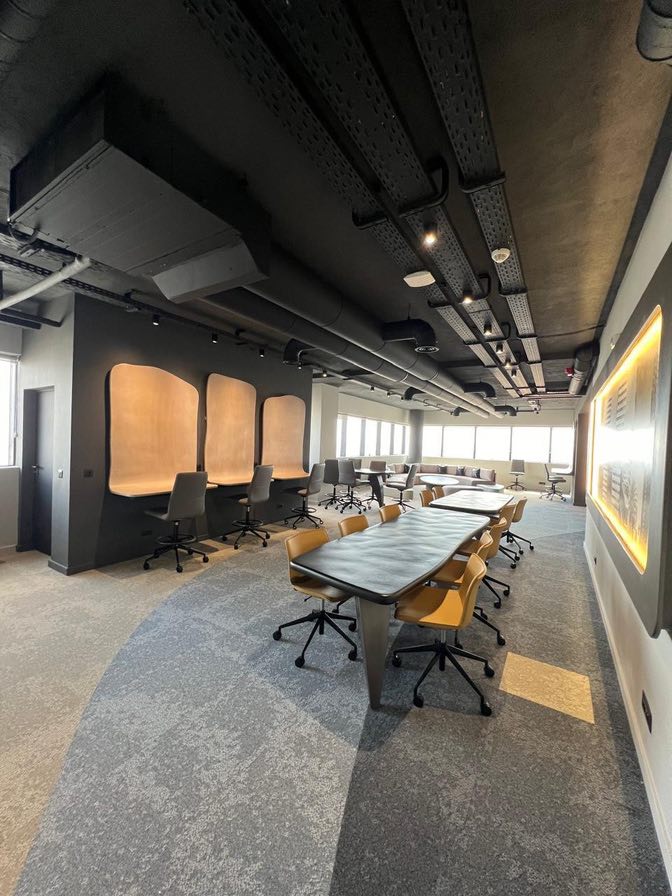 Salle de réunion avec plafond technique noir apparent, table de réunion et alcôves de travail individuelles éclairées, réalisation TG2A 23